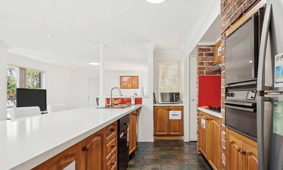 Long galley-style kitchen with white countertop, wooden cabinetry, and stainless-steel appliances.