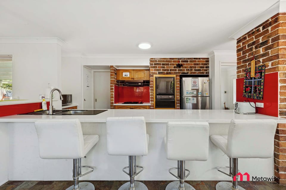 Contemporary kitchen with island bench, white bar stools, and brick feature wall.