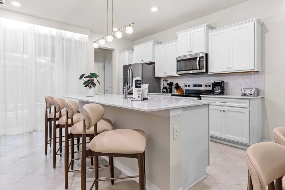This bright kitchen, with its sleek white cabinetry and marble countertops, inspires culinary creativity. Cozy bar stools are ideal for casual gatherings, while natural light fills the space, creating an inviting atmosphere.