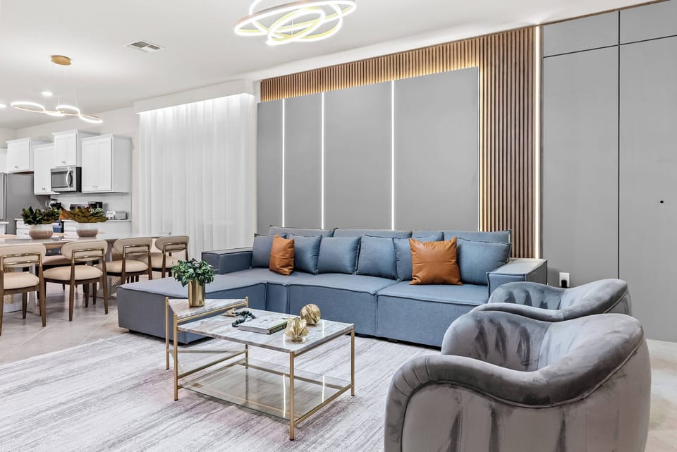 Enjoy a stylish living space with a plush blue sectional and warm orange pillows for a cozy feel. A sleek gold coffee table enhances the modern touch, while soft ambient lighting invites you to relax and unwind.