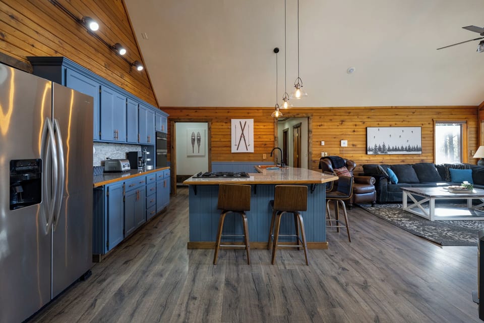 Your stunning open kitchen flows seamlessly into the cozy living area, featuring blue cabinetry, rustic wood accents, and modern appliances for memorable mountain getaways.