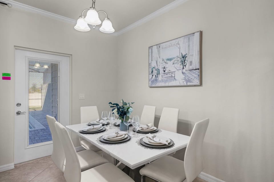 Bright dining nook seats six, with sleek white chairs, coastal art, and patio door access-perfect for family meals.