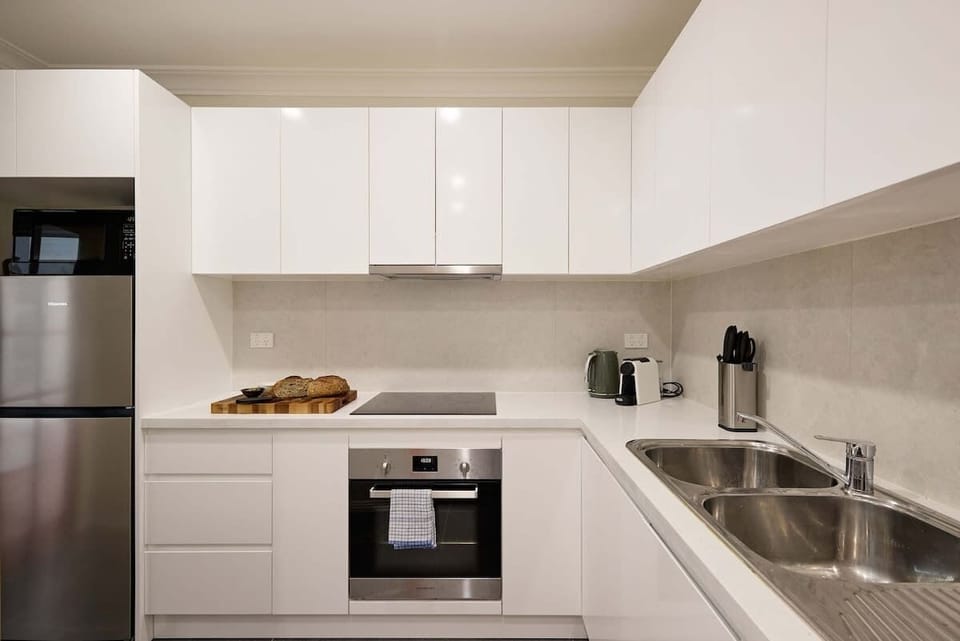 Modern Kitchen:
Sleek white kitchen featuring full-size appliances, generous prep space, and efficient layout. Everything you need for convenient meal preparation in your Surry Hills home away from home.