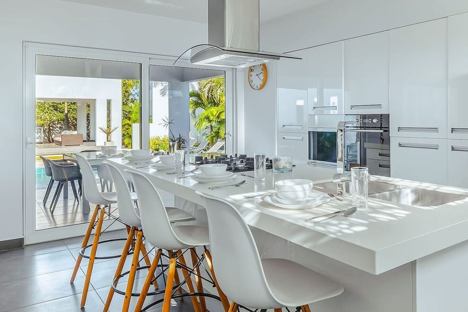 A bright, modern kitchen with a spacious island and bar seating—perfect for casual breakfasts, shared meals, and easy cooking with a view of the pool.