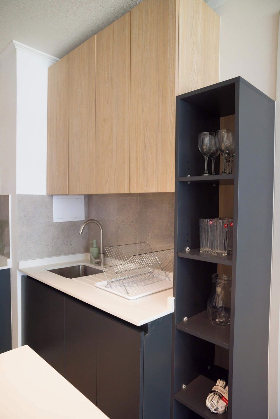 Compact kitchen with warm wood cabinetry, a stainless-steel sink, and glassware ready for guests.
