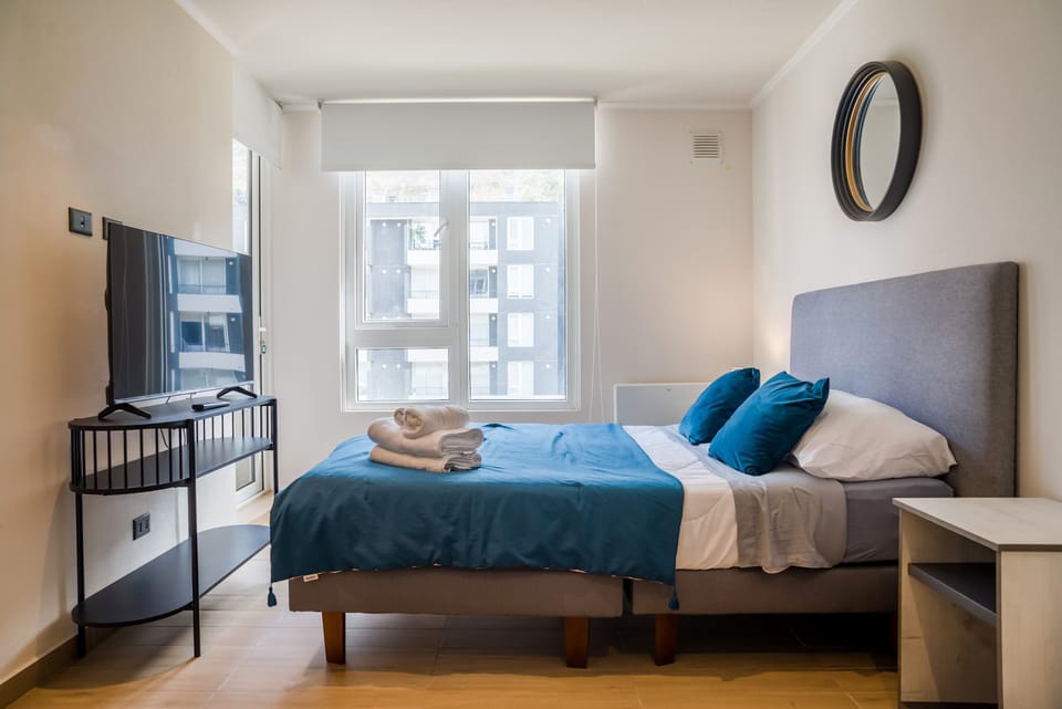 Private bedroom with a teal-accented bed, folded towels, and large windows that fill the room with natural daylight.