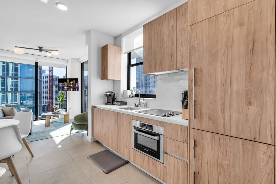 Gourmet Ready: Modern kitchen featuring sleek wood cabinetry, integrated high-end appliances, and stone countertops. Includes a built-in oven, stovetop, and a window that fills your cooking space with natural light