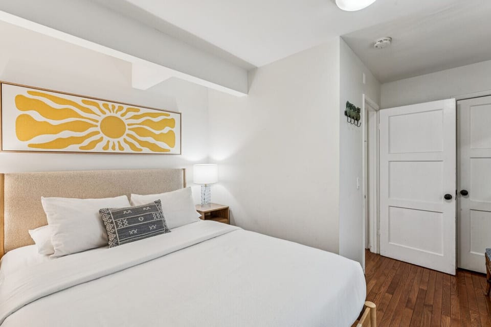 Simple bedroom w/ bed, warm wood floors & clean, minimal decor