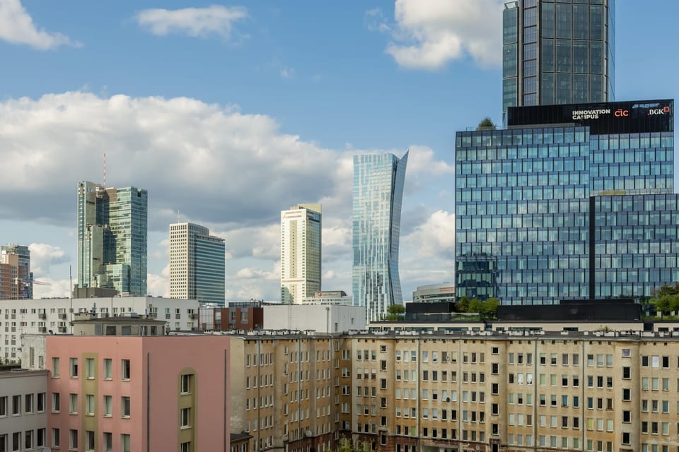 A wide panoramic view captures a city skyline where a striking, curved glass tower and other modern skyscrapers dominate the horizon under a bright sky. 