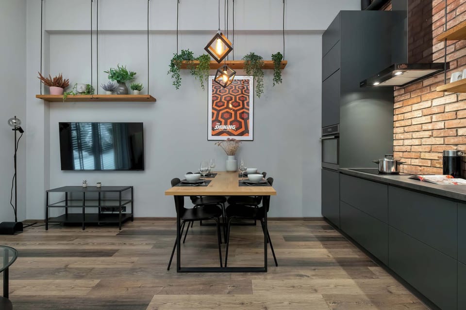 A stylish open-plan kitchen and dining area with dark cabinetry and a brick backsplash. A small dining table sits centrally, creating a cozy place for meals.