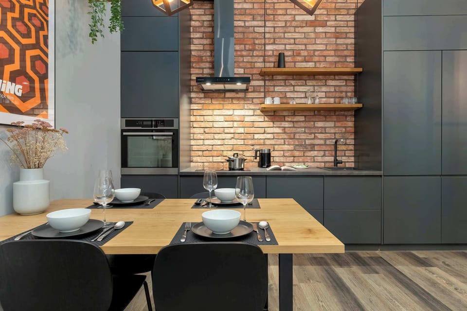 A dining table set in front of a brick-accent kitchen wall. The combination of wood and dark finishes creates a modern industrial feel.