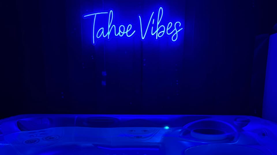 Soak in the glowing hot tub under neon 'Tahoe Vibes' lighting for the ultimate relaxation experience.
