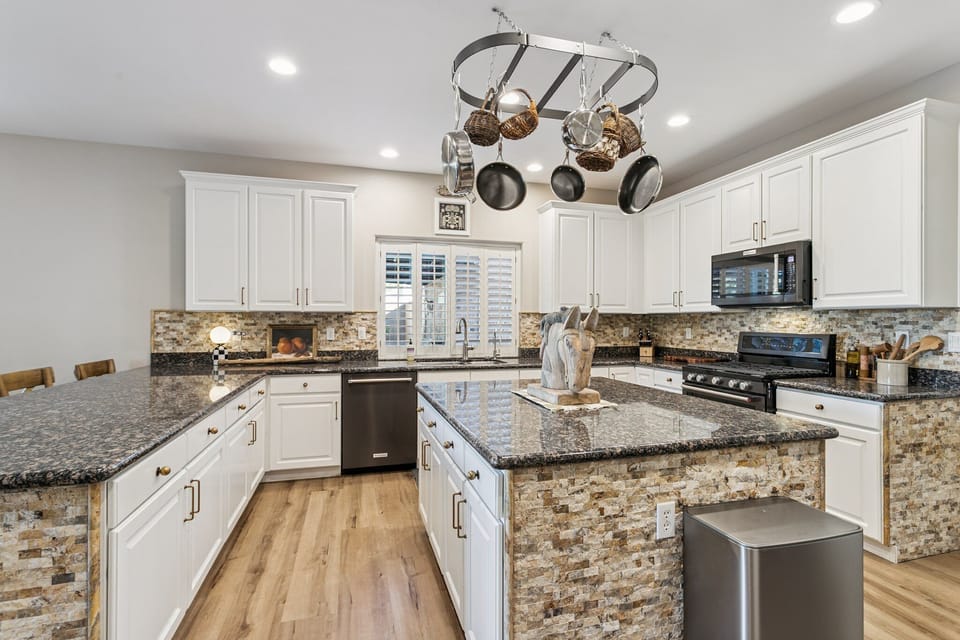 Your dream kitchen awaits with granite counters, white cabinetry, and a pot rack ready for culinary adventures.