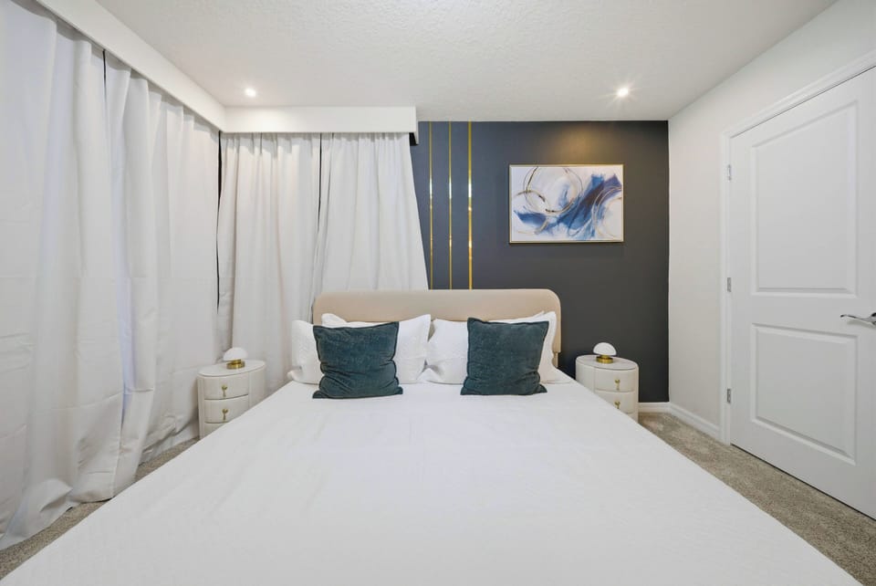 This cozy bedroom features a plush bed framed by soft, flowing curtains that create an airy ambiance. Accented with bold wall art and stylish nightstands, the space invites restful nights and rejuvenating mornings.