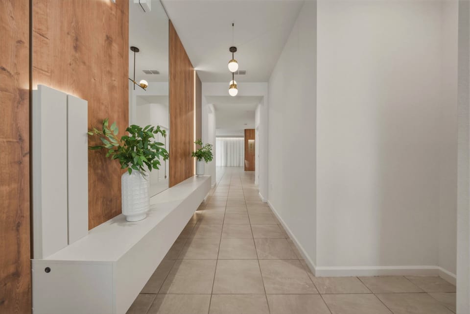 Enter a stylish corridor with warm wooden accents and sleek white walls. The polished tiles reflect soft lighting, and a minimalist bench invites you to pause and enjoy the refreshing greenery around you.