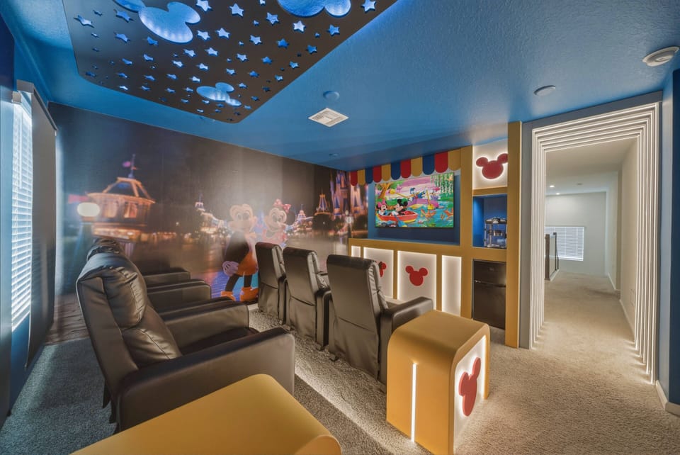 Step into a vibrant entertainment room featuring plush black recliners and a playful blue ceiling adorned with twinkling lights. With colorful wall art and a cozy layout, this space is perfect for movie nights and family fun.