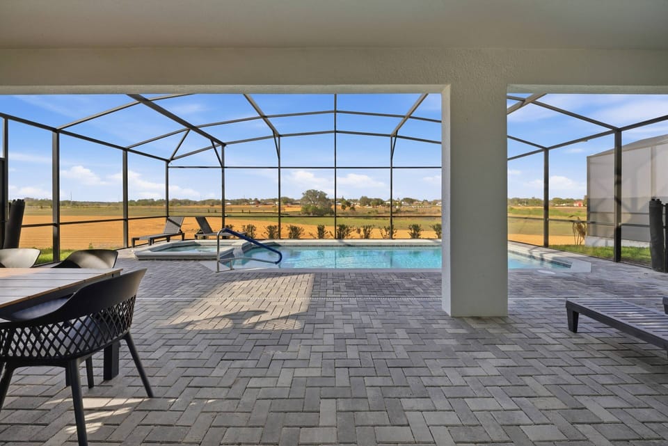 Enter a bright, airy space that opens to your private pool area with large screens for stunning views of the landscape. The patio boasts stylish black chairs and a spacious layout, ideal for your relaxation.