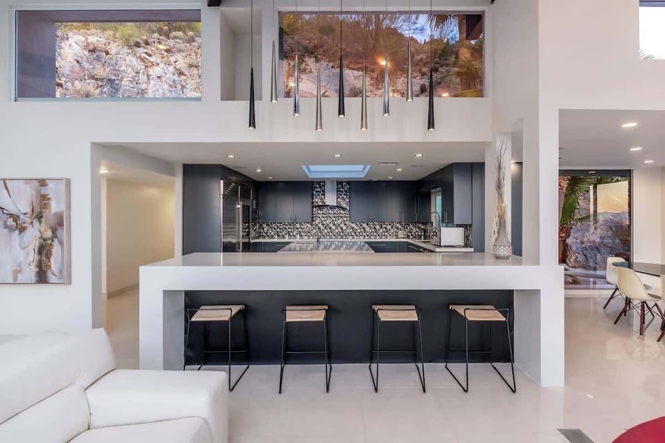 Modern luxury unfolds in this sleek open-plan space where your gourmet kitchen, illuminated living area, and dramatic hillside views create the perfect backdrop for unforgettable moments.