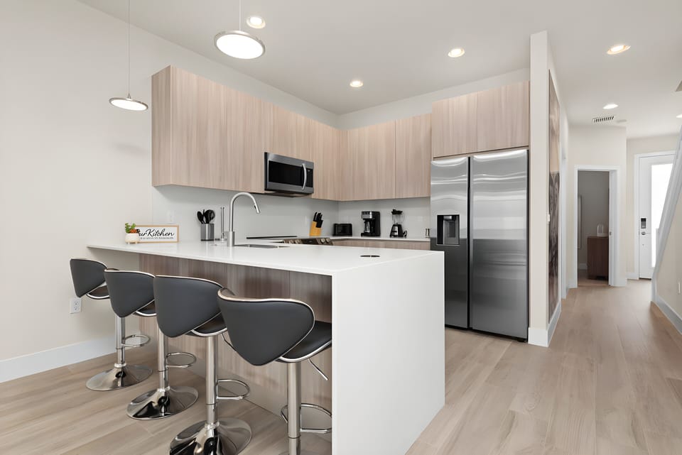 Welcome to a contemporary kitchen with sleek wood cabinetry and a spacious island with stylish bar stools, perfect for casual dining. Modern amenities and bright lighting create an inviting atmosphere for your culinary adventures.