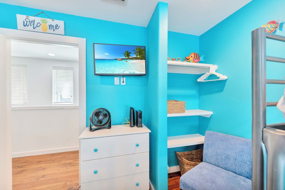 Relax in your bright beach-themed retreat with turquoise walls, tropical TV scenery, and cozy seating for peaceful moments.