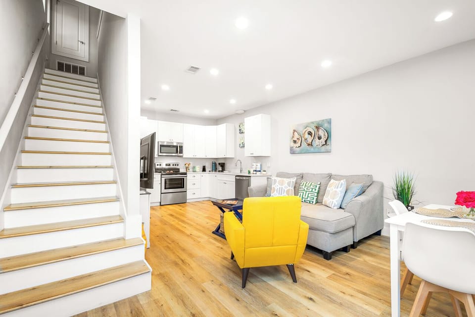 Step into your stylish open-plan retreat where warm hardwood floors flow beneath soaring white ceilings, connecting the modern kitchen to your bright living area.