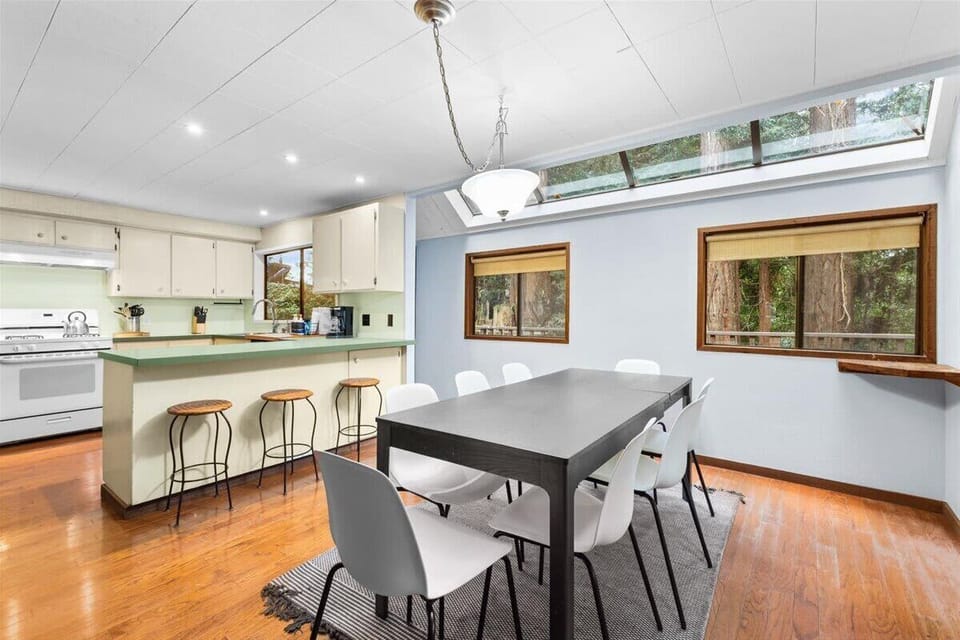 Bright dining area with forest views, skylights, and seating for 8 near the kitchen bar.