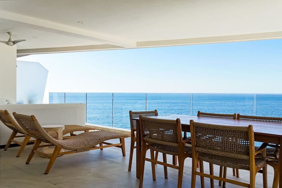 This outdoor living space features woven lounge chairs and a wooden dining table, creating a cozy and stylish retreat. The area seamlessly connects to the indoor living room through floor-to-ceiling sliding glass doors.