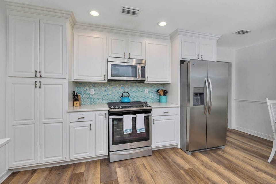Main House Kitchen with Full Appliances - Full kitchen with stainless appliances, white cabinetry, tile backsplash, and wood floors near the living room.