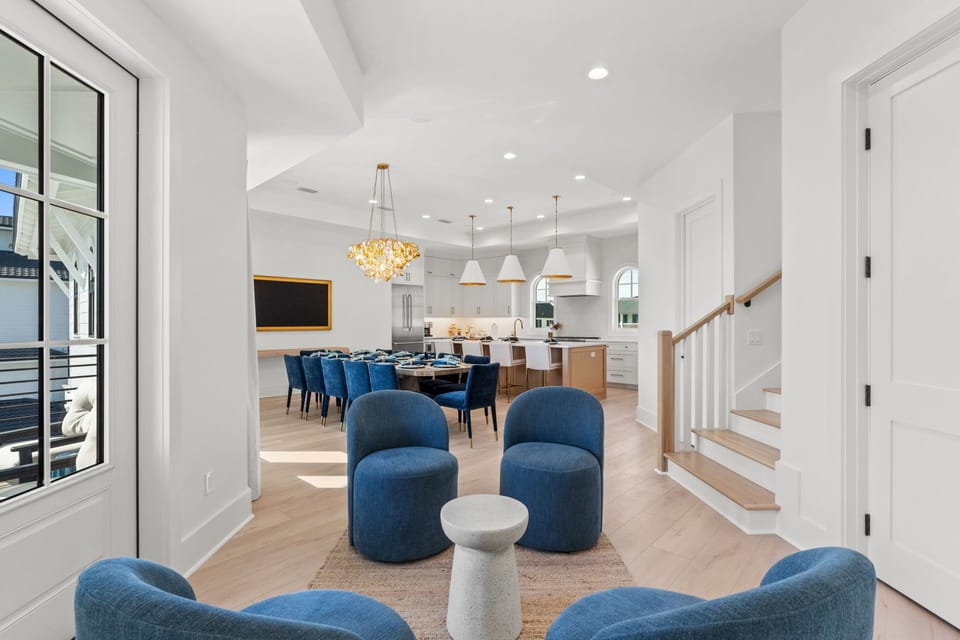 Relax in your spacious open-concept living area with plush blue seating and elegant chandelier, flowing seamlessly into your gourmet kitchen.