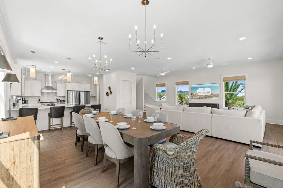 Gather around the dining table in this bright, open-concept living space where coastal charm meets modern comfort. Natural light and views of palm trees create the perfect setting to relax and make memories together.