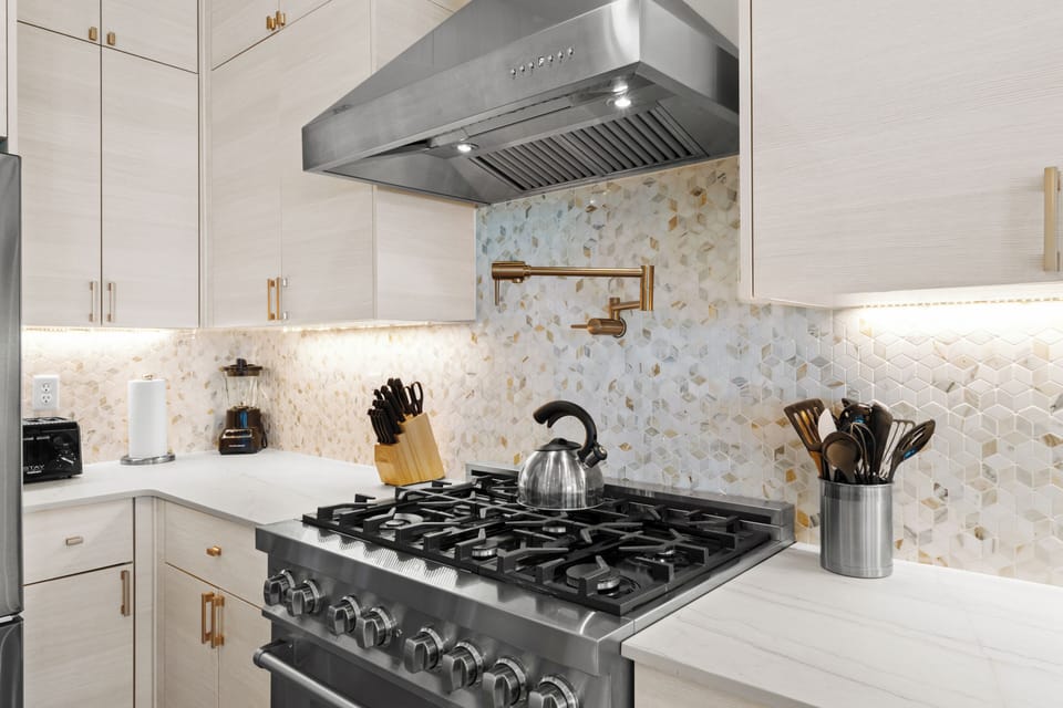 Your gourmet kitchen features a professional-grade gas stove and gleaming stainless steel range hood, all set against stunning mosaic tile backsplash with warm metallic accents.