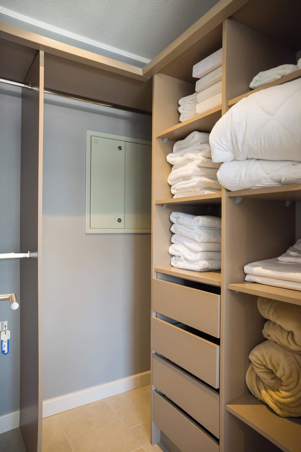 Bedroom with crisp white bedding and built-in shelving stocked with neatly folded linens.