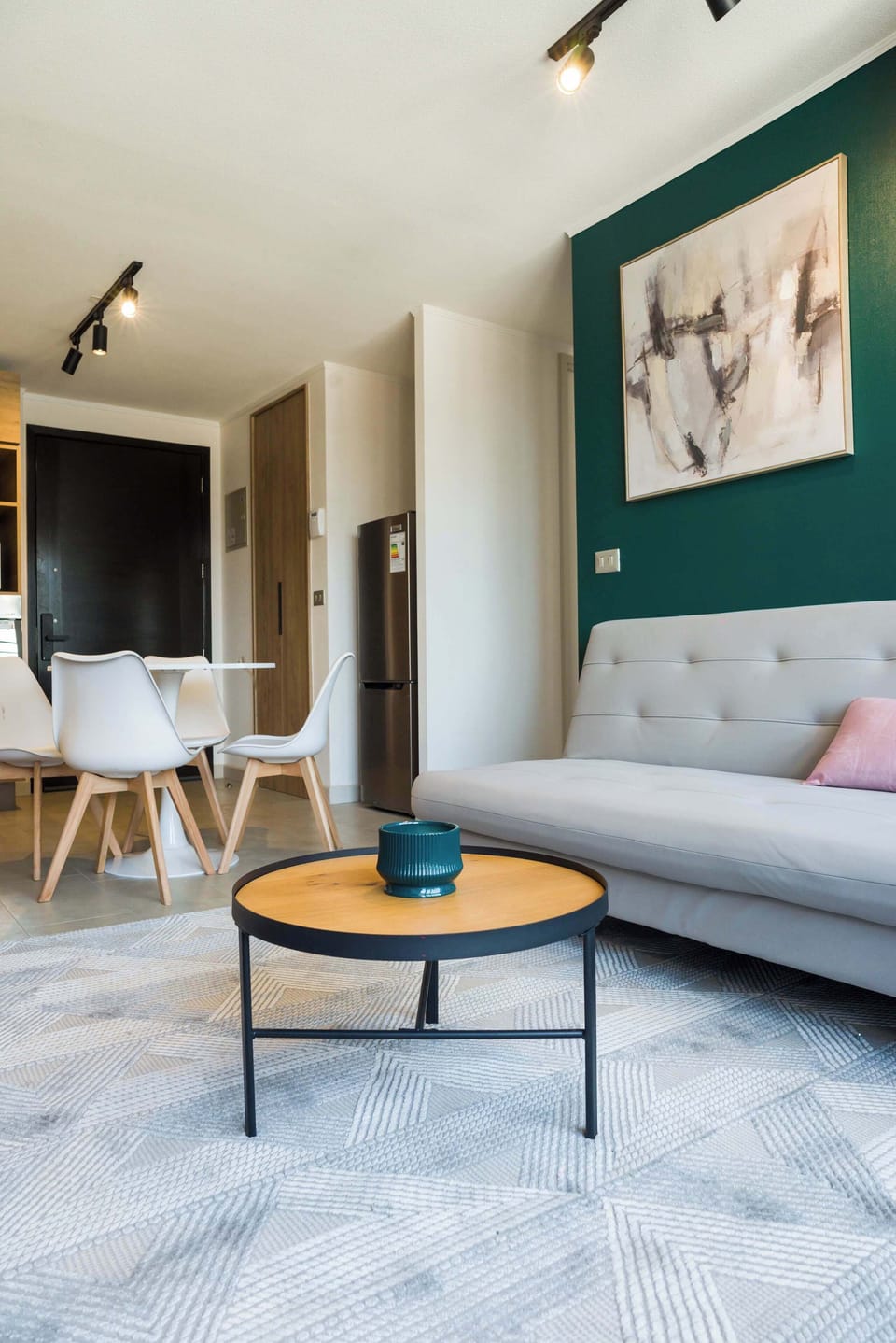 Open-plan living room with a white sectional, round wood coffee table, and teal accent wall with abstract artwork.