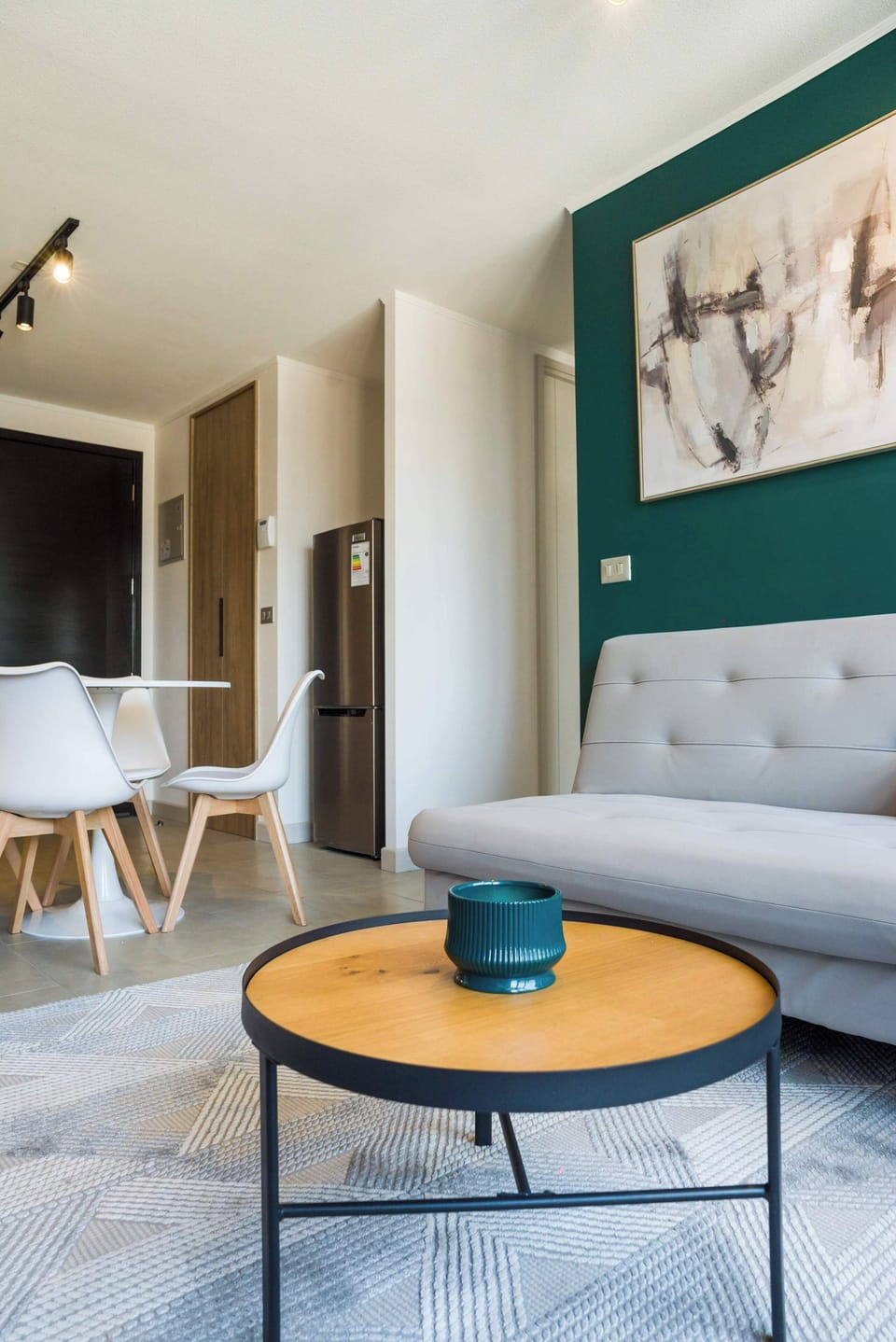 Living room with a light-gray sectional, round wood coffee table, and bold teal accent wall beside the dining area.