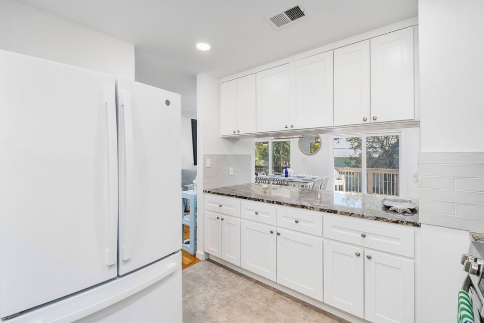 Cook your favorite meals in this bright, fully equipped kitchen with granite countertops, crisp white cabinetry, and serene water views through the window—perfect for your morning coffee or evening prep.