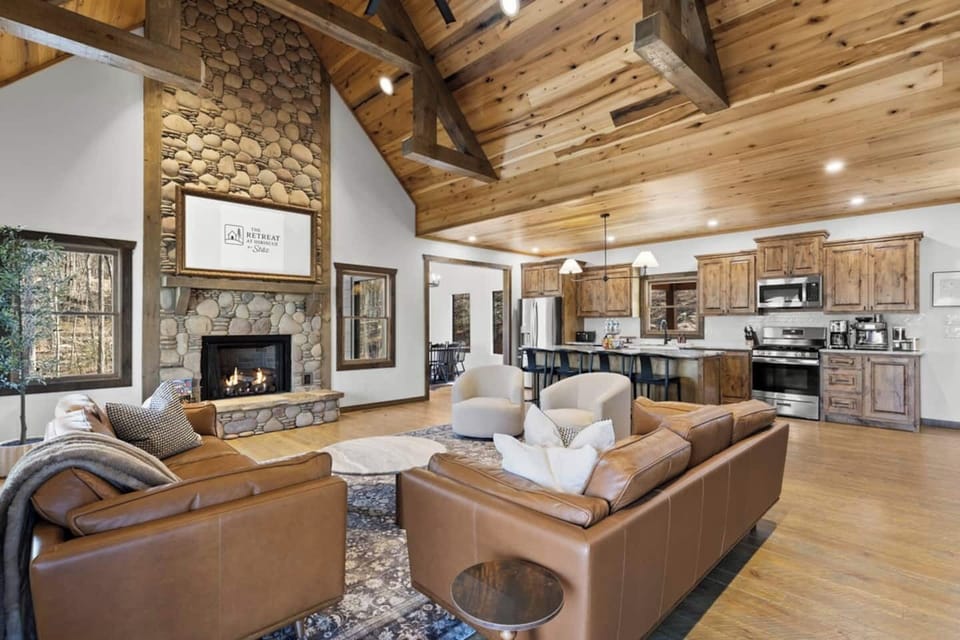 Beautiful open-concept living area with a statement stone fireplace, warm wood finishes, and ample seating, creating an inviting space for connection and comfort.