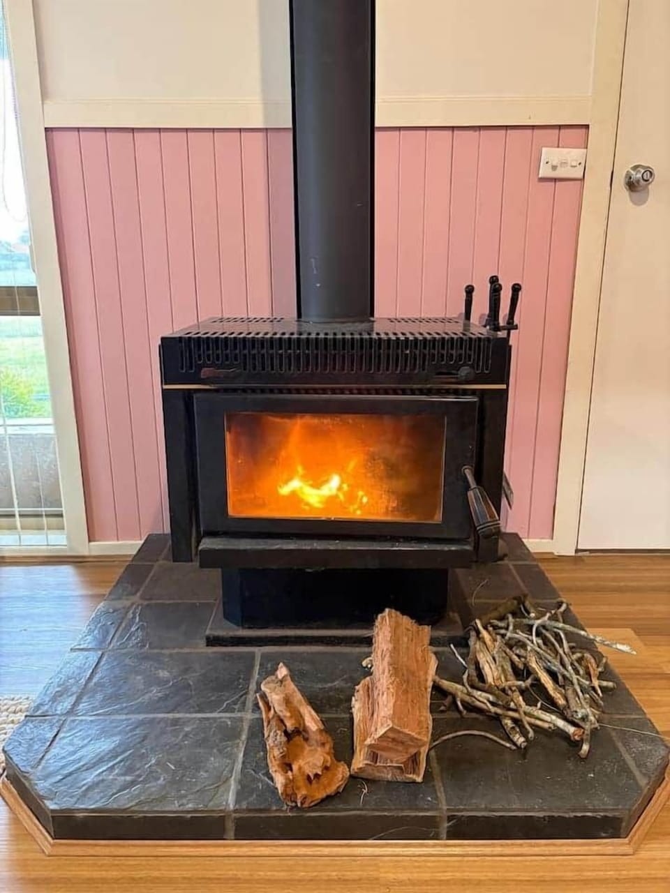 The main living room features a 75 inch TCL television, A/C, a comfortable 3 seater linen lounge, a coffee table, wood fireplace, dimmable LED downlights and sheer curtains. There is also a hallway door which allows privacy from the bedroom wing.