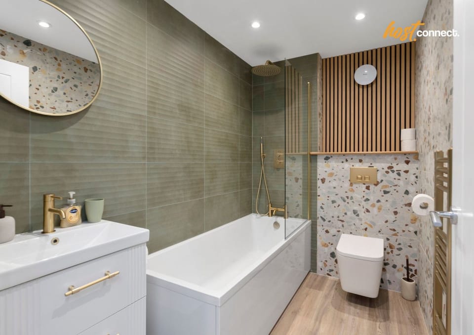 Experience a touch of our stunning bathroom, featuring stylish terrazzo-style tiling and  gold fixtures. This contemporary space includes a full-sized bath with a sleek gold mixer tap and a high-pressure shower with a handheld attachment, perfect for a lo