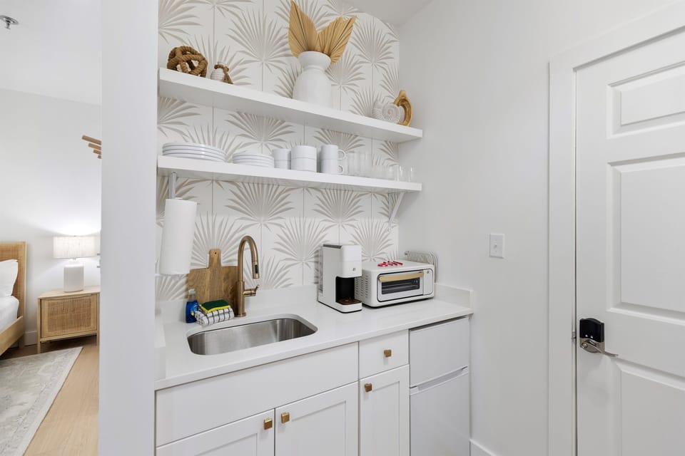 Your stylish kitchenette features elegant palm-patterned tiles, open shelving with curated accessories, and modern appliances for effortless meal prep.