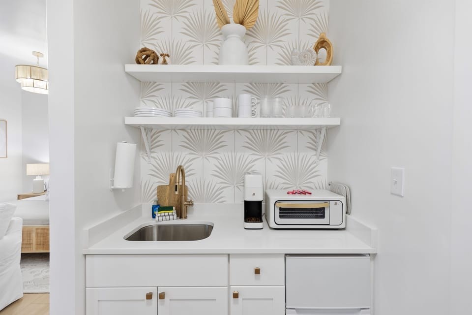 Your stylish kitchenette features elegant palm-leaf wallpaper, modern appliances, and floating shelves with coastal-inspired décor for effortless meal prep.