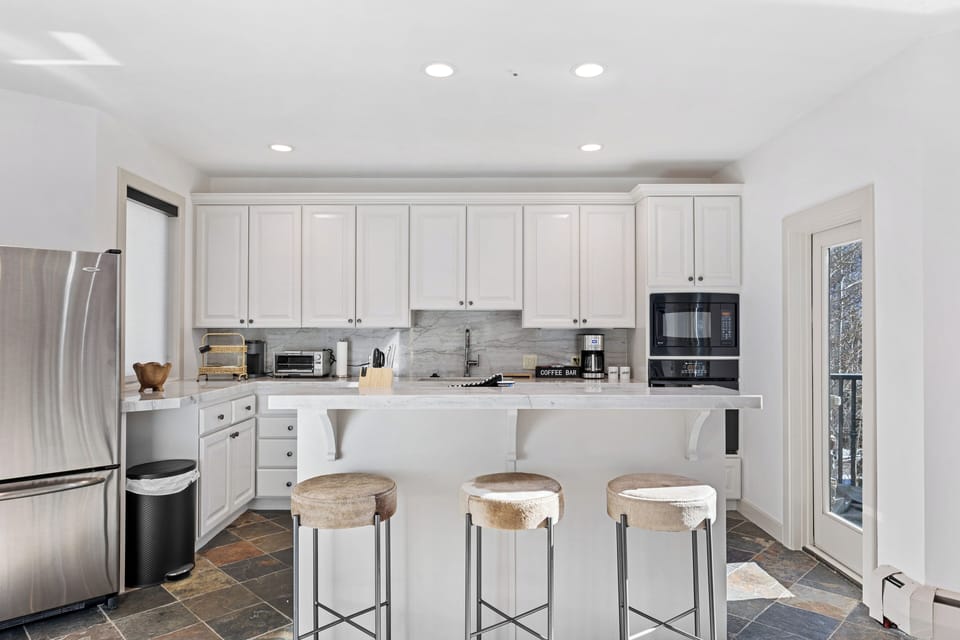 Bright main-floor kitchen featuring stainless steel appliances, generous counter space, and bar seating. Convenient access to the laundry room and a door leading to the private deck.
