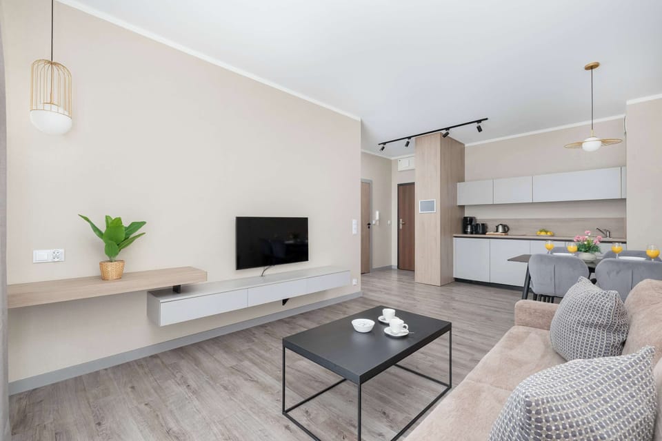 A modern living room with a wall-mounted TV and open shelving. The layout is minimal and uncluttered.