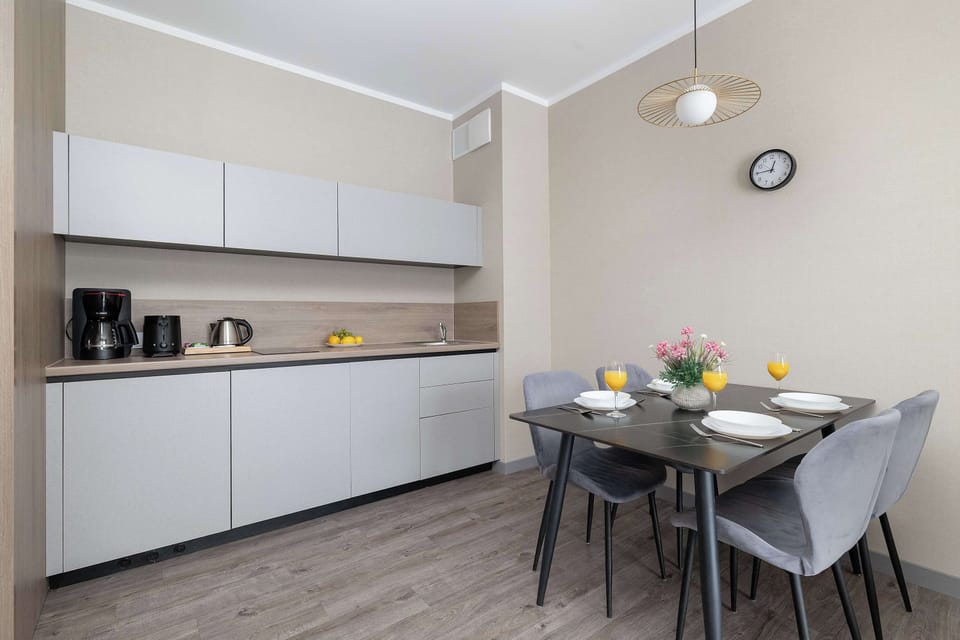 A minimalist dining area next to a sleek white kitchen. Clean lines and neutral tones give it a modern look.