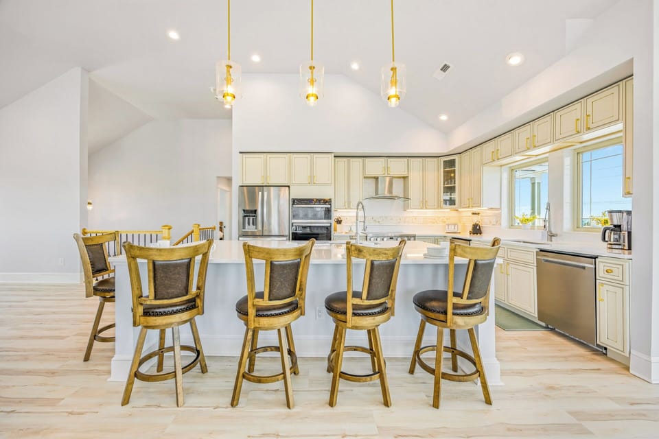 Gather around the bright kitchen island with seating for four, featuring cream cabinetry, stainless appliances, and vaulted ceilings with stylish pendant lighting—perfect for your morning coffee or meal prep.
