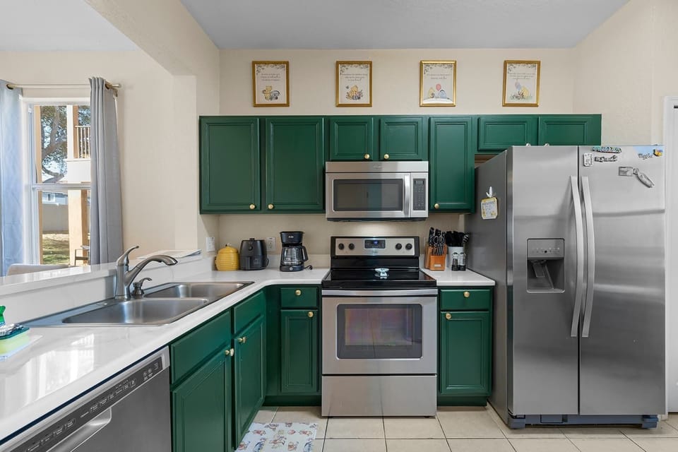 Kitchen w/ green cabinetry, stainless steel fridge & sink — functional & stylish.
