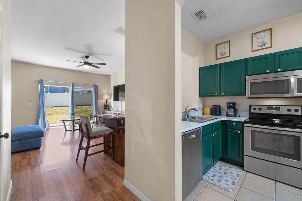 Kitchen w/ green cabinetry, stainless steel appliances & a view to the outdoor space.
