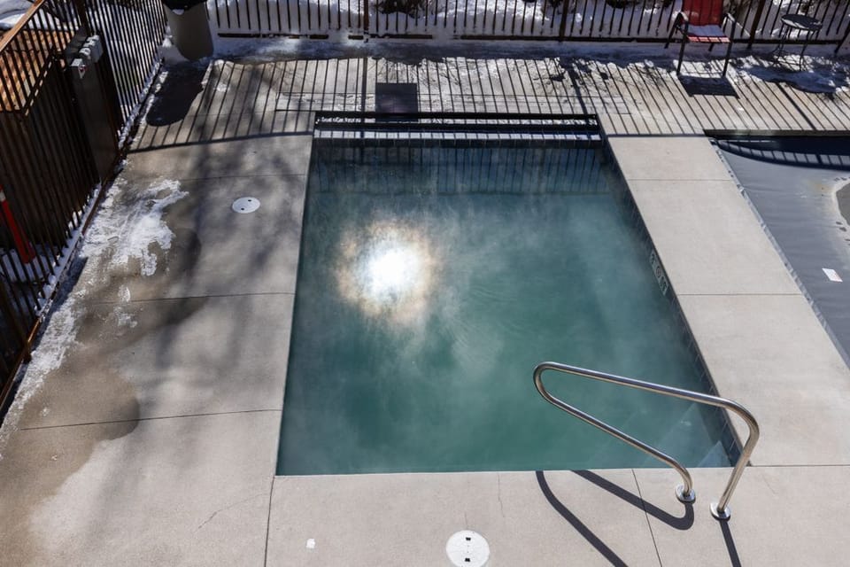 Steaming outdoor hot tub set into a concrete patio with surrounding snow.
