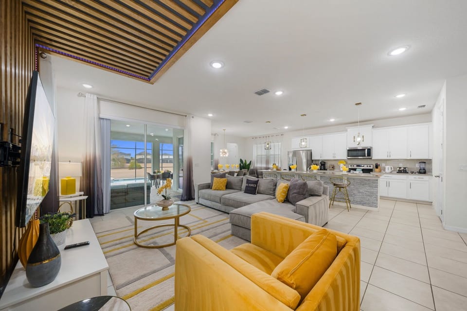 Relax in this open-plan living area with a plush sectional, mustard accent chair and wood-slat media wall-sliding doors open to the screened pool for effortless indoor-outdoor living.