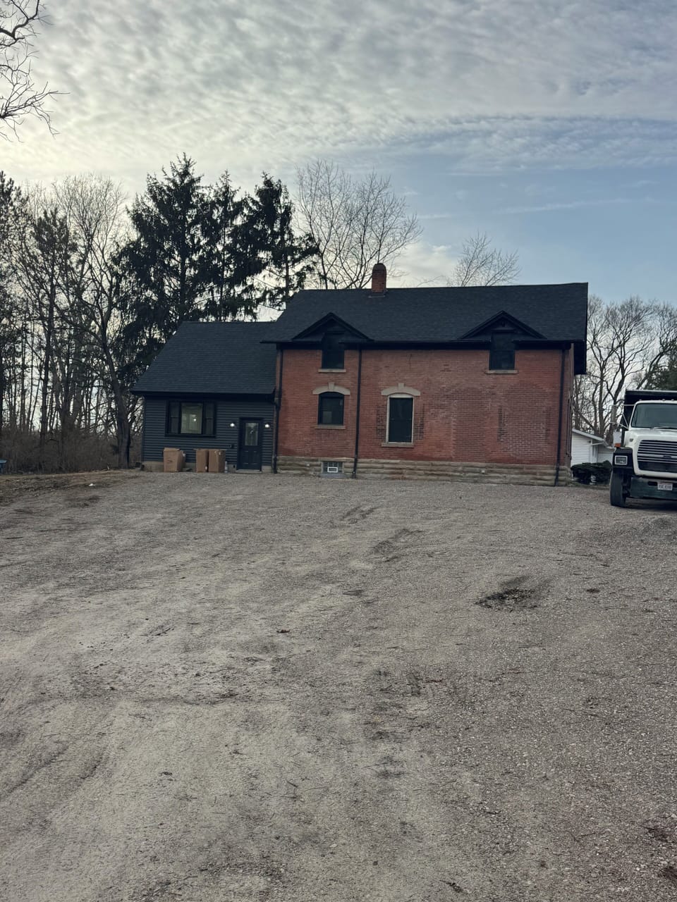 Charming property featuring brick and dark siding exterior with spacious open grounds and mature trees.