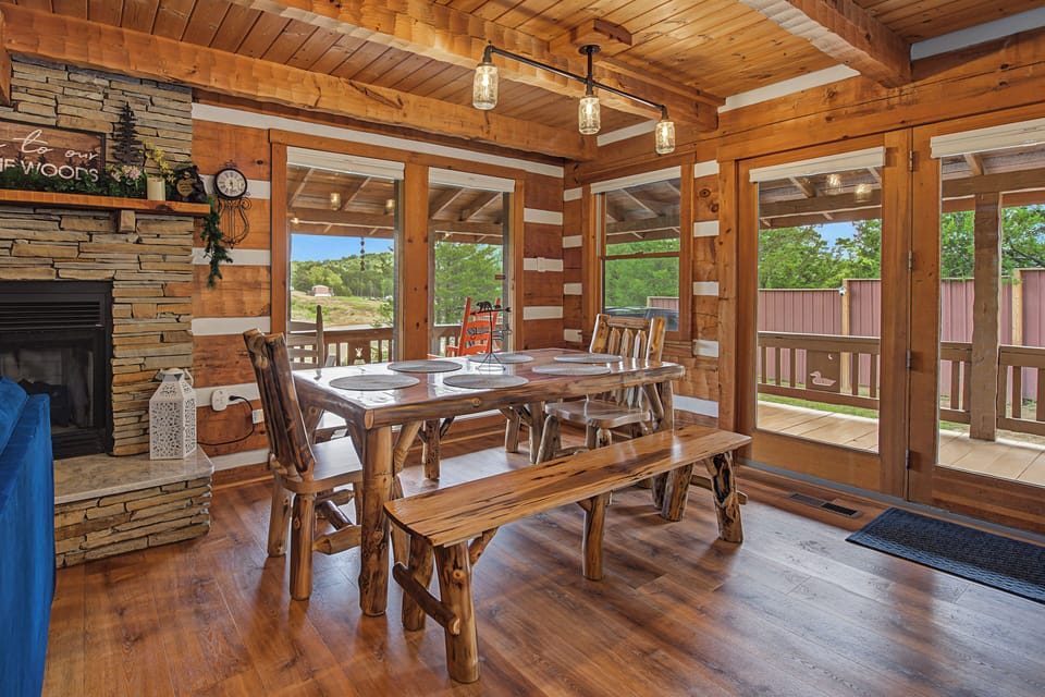 Gather around this handcrafted log dining table where your group can share meals and laughter. Rustic wood beams overhead, a stone fireplace, and expansive windows framing forest views create a warm, inviting mountain retreat.